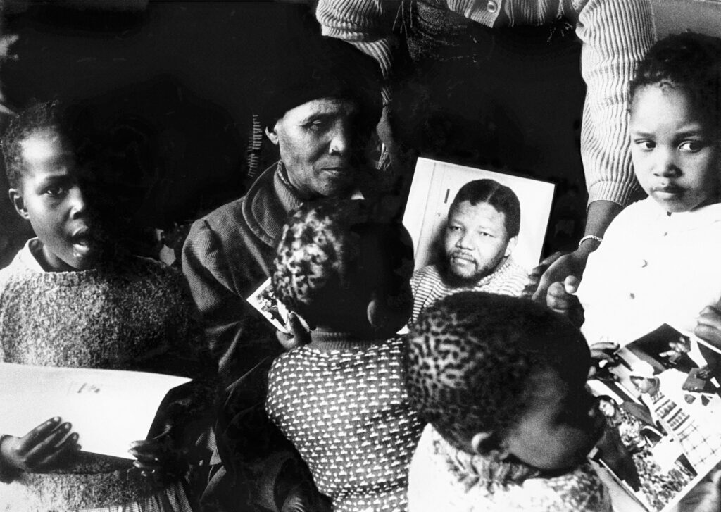 <p>A mother remembers. Noqaphi Nosekeni (Nelson Mandela’s mother) speaks to her grandchildren while holding a picture of her imprisoned son. <em>© Alf Kumalo Estate</em></p>
