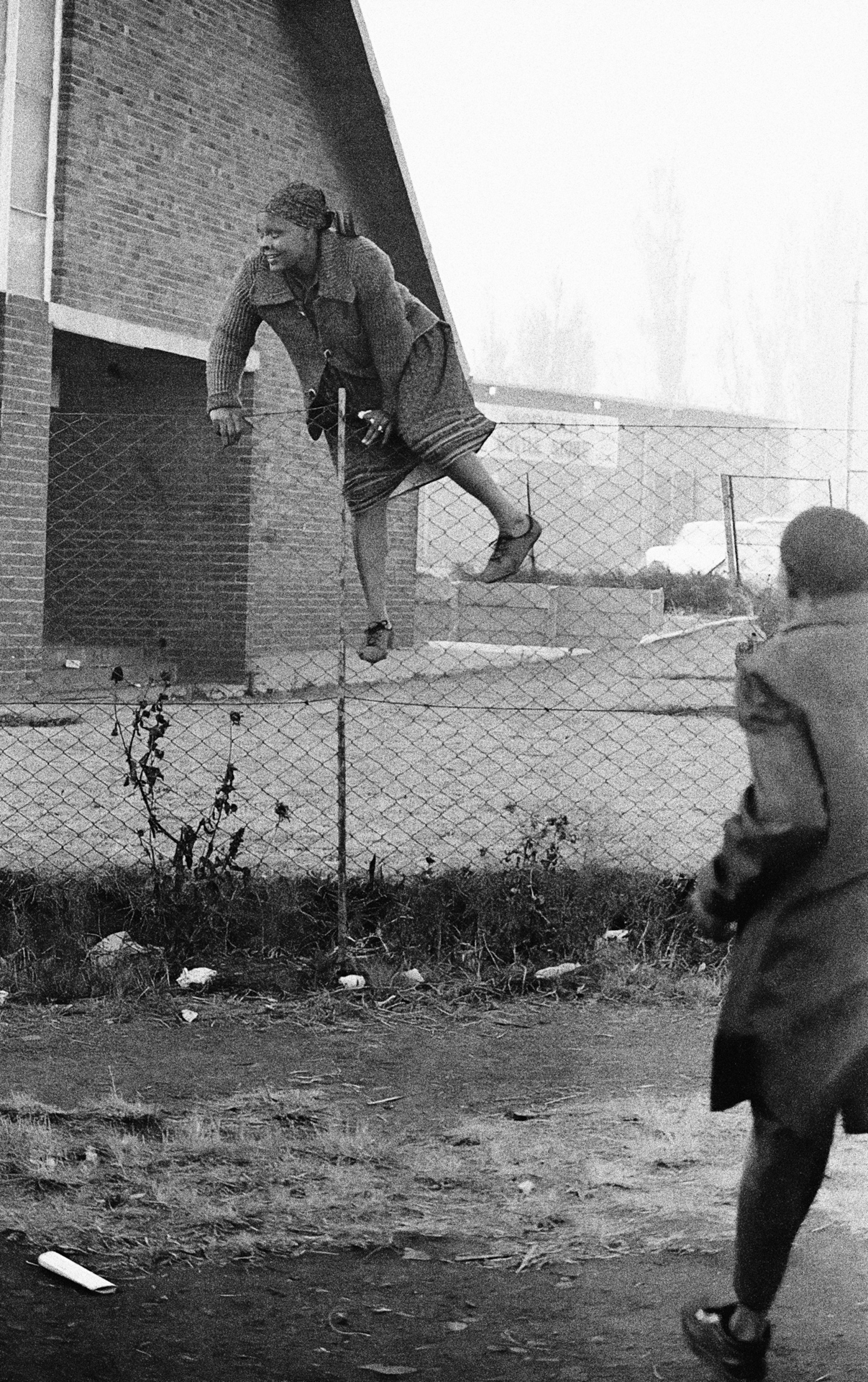 A woman climbs the fence to escape a police crack down at the Regina Mundi church in Soweto c.1985 © Alf Kumalo Estate