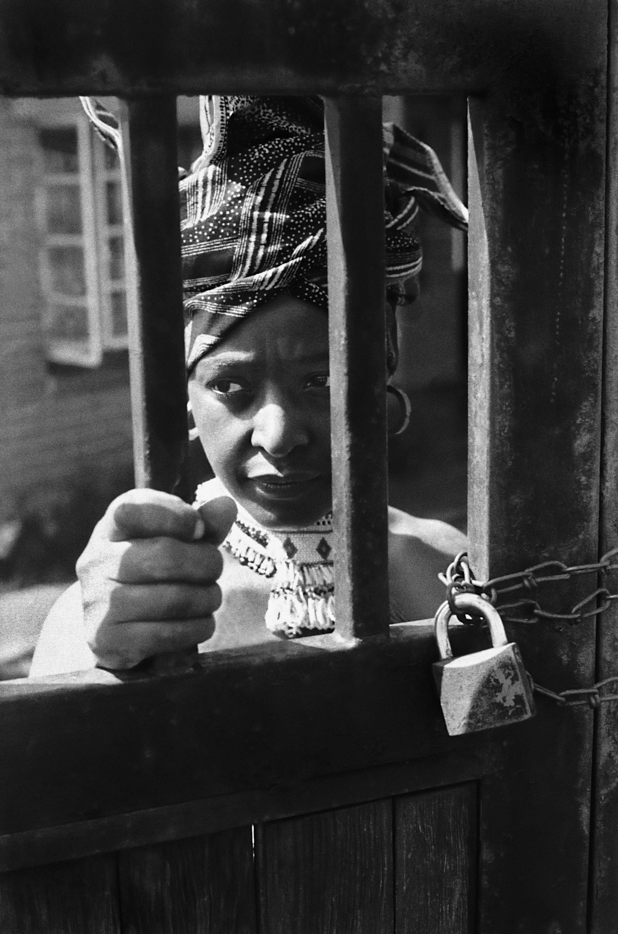 Winnie Mandela under house arrest behind the gate of her famous house in Soweto. © Alf Kumalo Estate