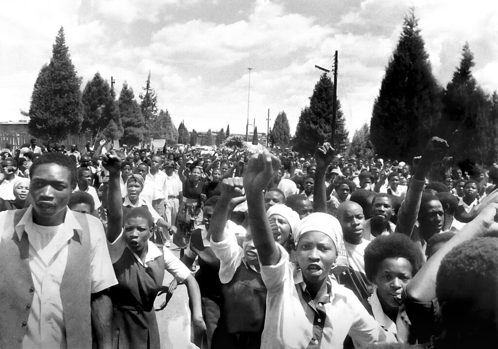 <p>Young mourners, enraged by the massacre of 16 June, march at the Doornkop Cemetery in Soweto at the burial of the victims. <em>© Alf Kumalo Estate</em></p>
